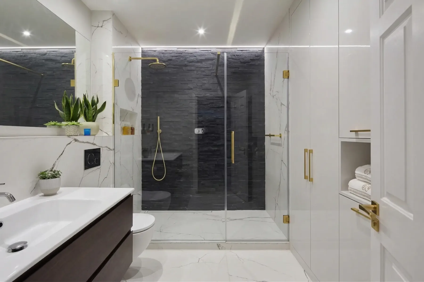 Bathroom with built-in shelving, a wide mirror and brass shower fittings